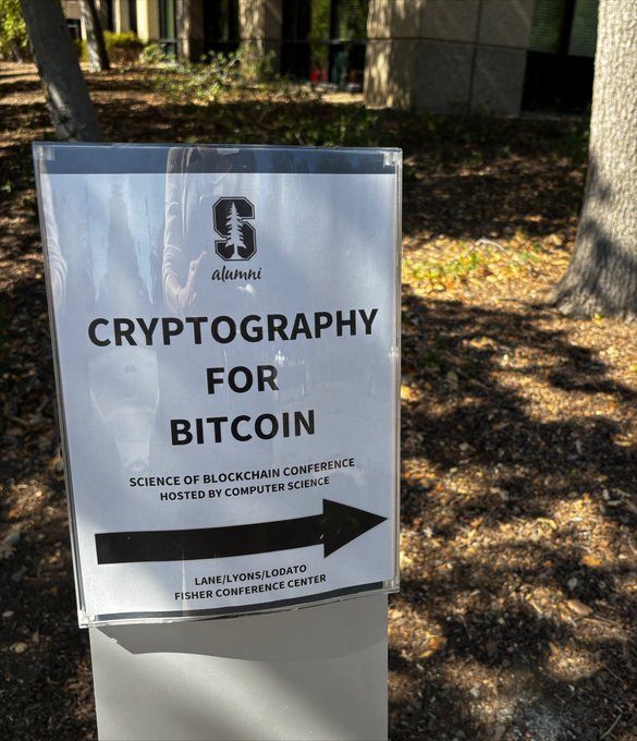 A sign outside the Stanford Alumni center advertises the "Science of Blockchain Conference" featuring a "Cryptography for Bitcoin" talk hosted by the Computer Science department at the Lane/Lyons/Lodato Fisher Conference Center — clearly the conference the poster is attending today.