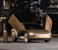 A futuristic gold-colored Tesla Cybercab vehicle with its doors open upward, parked on a city street at night with a person in beige standing nearby.
