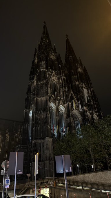 A towering Gothic cathedral, illuminated against the dark night sky, dominates the scene near what appears to be a roadway with signage. The majestic, spired silhouette reflects a sense of awe and finality, mirroring the contemplative "Goodnight" sentiment of the post.