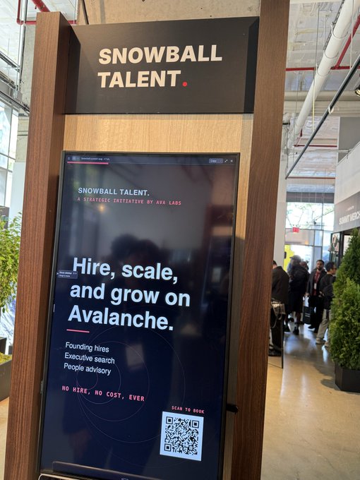A digital kiosk at what appears to be a conference displays an advertisement for "SNOWBALL TALENT," described as "A strategic initiative by Ava Labs," promoting services to "Hire, scale, and grow on Avalanche" with offerings including "Founding hires, Executive search, People advisory" and the slogan "NO HIRE, NO COST, EVER," alongside a QR code to book services—directly visualizing the post's announcement of Ava Labs' new recruiting agency dedicated to hiring for the Avalanche ecosystem.