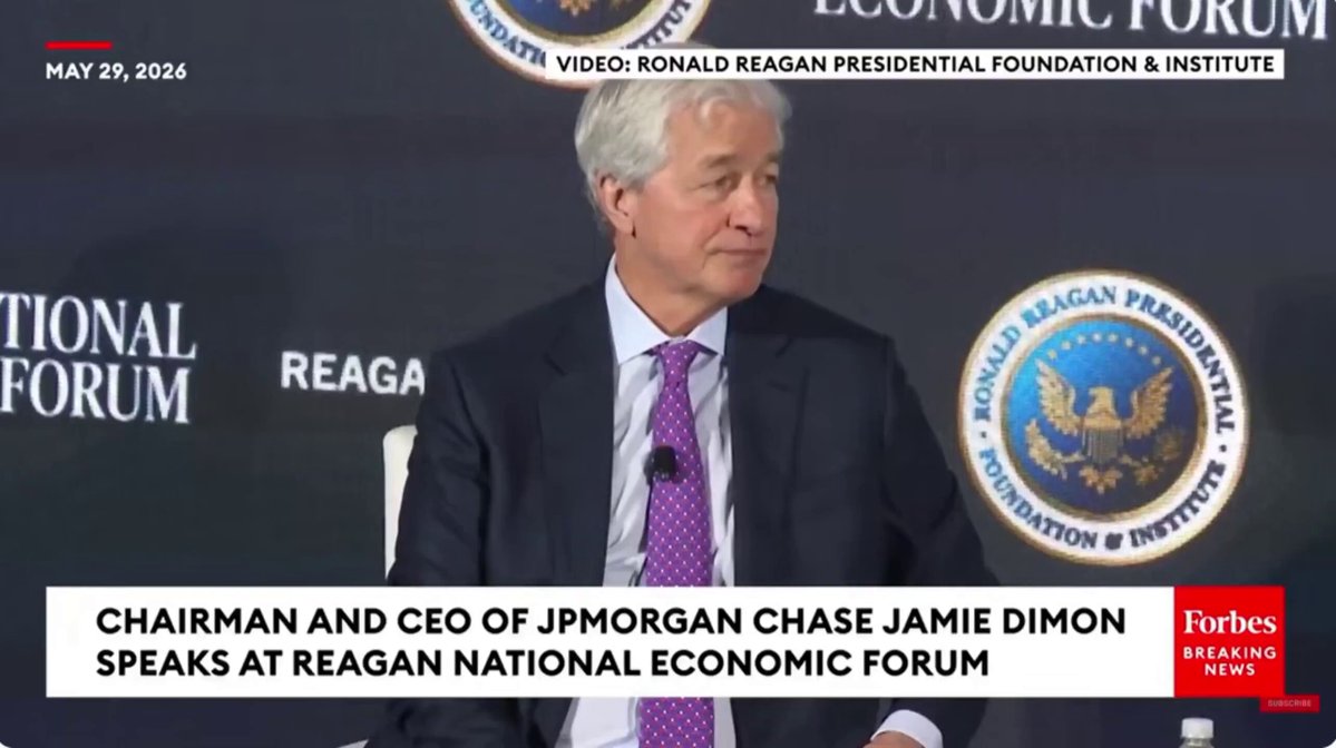 The image features a man sitting at a table, wearing a suit and tie. He appears to be giving a speech or presentation, as indicated by his body language and facial expressions. The text in the image suggests that he might be discussing Bitcoin and cryptocurrency, which are often associated with financial innovation and disruption.