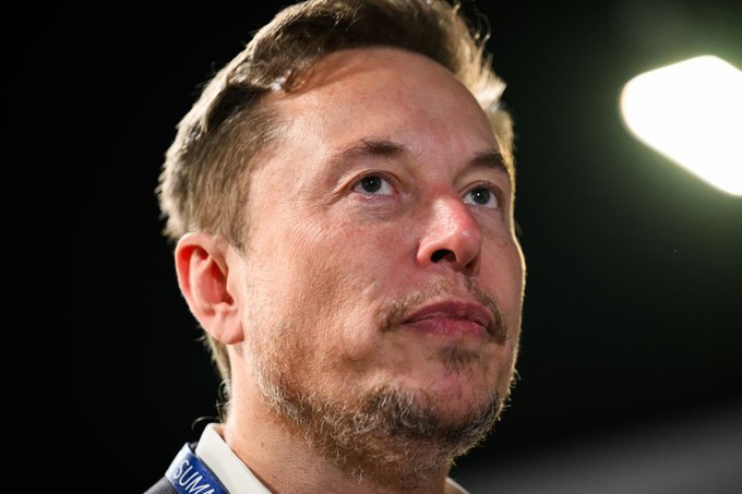 The image features a man with short hair, wearing a blue shirt, looking up at something off-camera. There are no other people or objects visible in the photo. The caption above the image reads "Elon Musk: I would like to see Bitcoin succeed." This suggests that the man might be discussing or contemplating the potential success of Bitcoin as an investment or cryptocurrency.