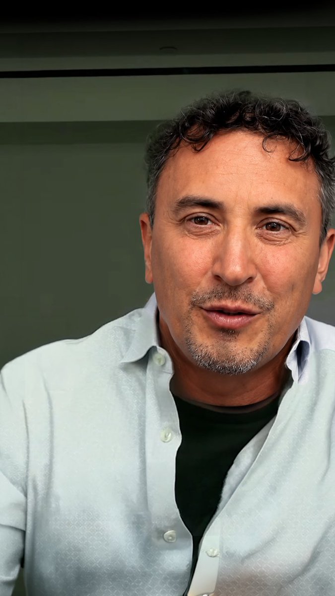 The image features a man wearing a white shirt with a green collar. He has curly hair and is looking directly at the camera while smiling. The background of the photo appears to be a green wall, which contrasts nicely with his white shirt. There are no texts or other objects in the image, so it seems like an advertisement for Avalanche.