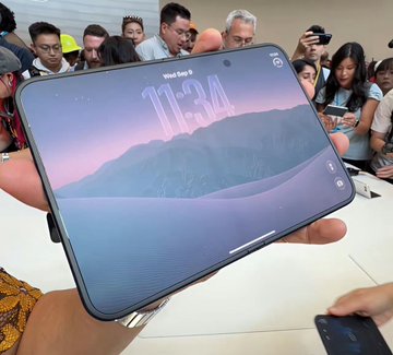 A large smartphone, resembling a Google Pixel, is held up to display its screen showing "Wed Sep 3" and "11:34" against a crowd of onlookers.