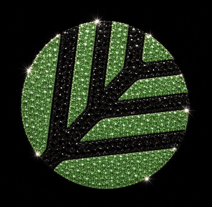 A sparkly green and black circular logo featuring stylized tree branch designs with starburst sparkles around the edges on a black background.