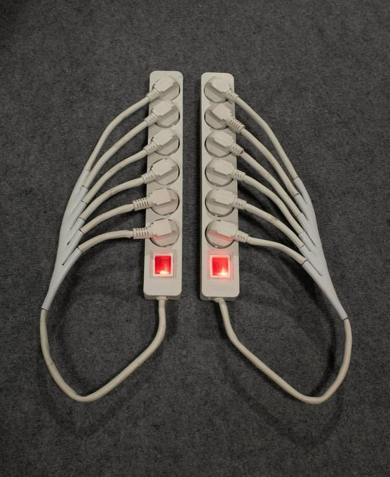A power strip shaped like angel wings with multiple outlets, switches, and a glowing red power indicator, displayed on a dark surface.