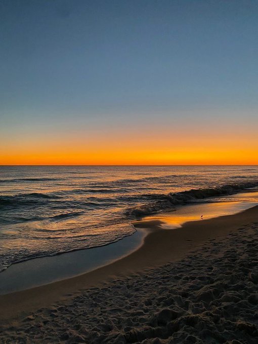 The image shows a beach at sunset with the ocean, sand, and sky creating a beautiful scene. There are footprints visible on the sandy shoreline, indicating that people have been enjoying their time there. The photo has been shared by @wallchain and @quipnetwork, who seem to be promoting or discussing the image. The post is titled "Good Night CT While most people are winding down", which suggests a sense of relaxation and leisure at the beach during sunset.