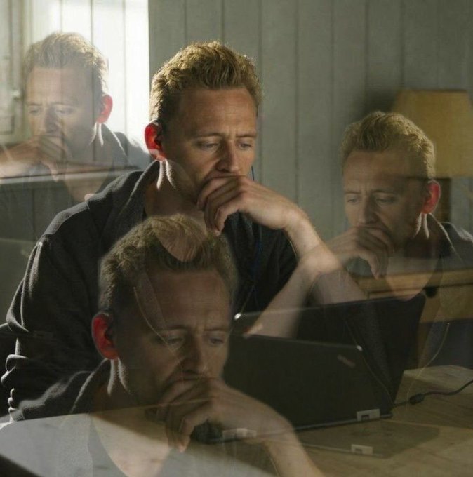 A contemplative-looking man sits in front of a laptop, with a multi-exposure effect creating overlapping reflections or ghosted images of his face in the foreground and background.
