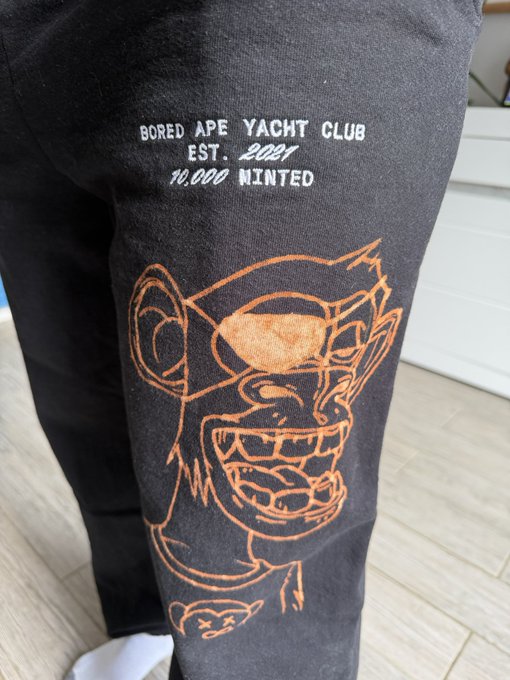 A person wearing black pants featuring an orange printed graphic of a Bored Ape and the text 'BORED APE YACHT CLUB EST. 2021 10,000 MINTED'.
