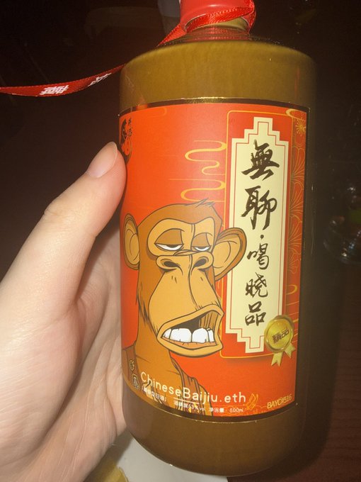 A hand holds a bottle of Chinese Baijiu featuring a cartoon ape illustration and the text "無聊·唱烧品" with a BAYC (Bored Ape Yacht Club) tag, celebrating a meetup with fellow NFT collectors at the BAYC Hong Kong Station event.