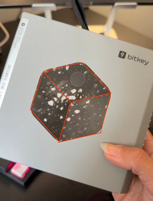 A hand holding a silver Bitkey device box featuring a speckled 3D cube graphic and the text 'SECURED. FOR LIFE.'