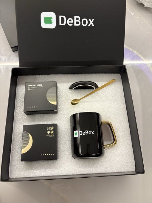 A DeBox gift set is presented in a black box, featuring two "Moon Light" Mid-Autumn Festival gift boxes, a black DeBox mug with a gold handle, and a gold spoon. The elegant packaging with its lunar-themed design celebrates the Mid-Autumn Festival, complementing the post's grateful mention of receiving a surprise from DeBox.