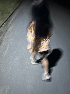 The image shows a person wearing black shorts, running down a street at night with their shadow visible behind them. The photo appears blurry due to motion blur, which suggests that the subject was moving quickly while taking the picture. The caption provided after the image reads "娘と夜ラン！ 小1の娘に一緒に走りたいって走らせたら 1エナを時速7km越えで走れてびっくり #STEPN #STEPNGO".
