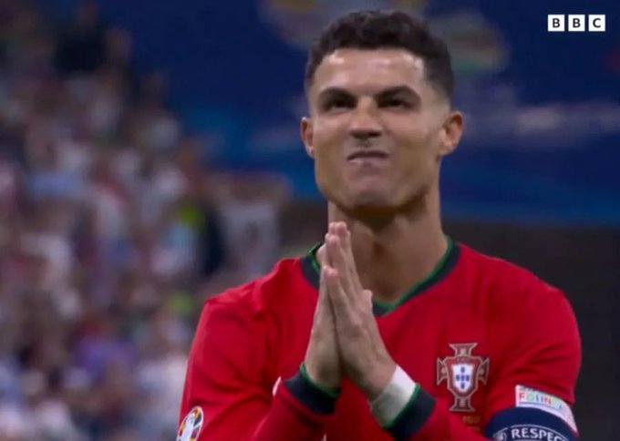 Portuguese footballer Cristiano Ronaldo, wearing the red Portugal national team jersey, presses his hands together in a prayer-like gesture during a match broadcast by the BBC.