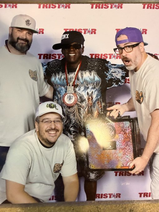 Four people pose together at a TRISTAR event, with one holding a large decorative box, appearing to celebrate a win or achievement.