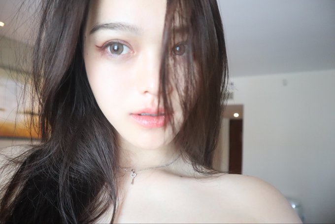 A close-up selfie of a young woman with long dark hair, fair skin, and pink lips, wearing a delicate silver necklace. The image accompanies a classical Chinese proverb about perseverance and determination, with the woman's calm, resolute gaze embodying the spirit of unwavering resolve described in the text.