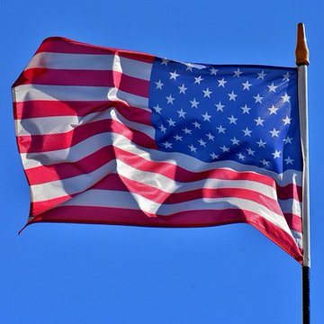 An American flag waves against a clear blue sky, attached to a silver flagpole.