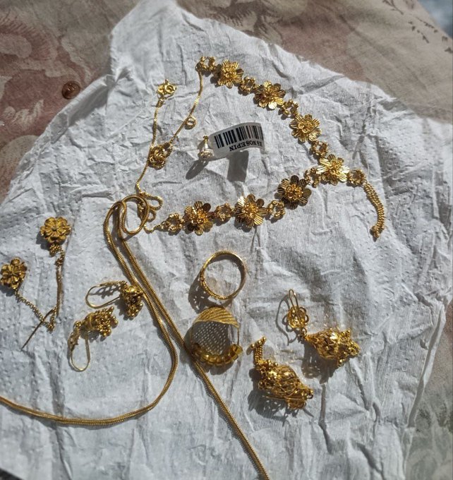 A woman displays an extensive collection of gold jewelry including floral necklaces, chains, rings, and earrings arranged on white fabric, with a "MISSGUIDED" clothing tag visible. The image relates to the post by showcasing the luxurious gold pieces likely purchased using cryptocurrency airdrop earnings, fulfilling the achievement of buying gold for her mother.