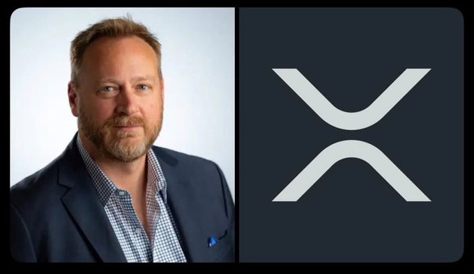 A man with a beard wearing a blue blazer and checkered shirt posing for a portrait next to a large white XRP logo on a dark background.