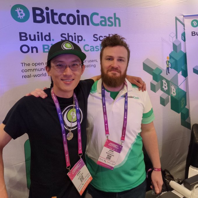 Two smiling attendees pose in front of a Bitcoin Cash booth at the Futurist Conference, with one wearing a branded "Bitcoin Cash" polo and lanyard reading "Fink @BitcoinCash" while the backdrop displays "Bitcoin Cash - Build. Ship. Scale On Bitcoin Cash."
