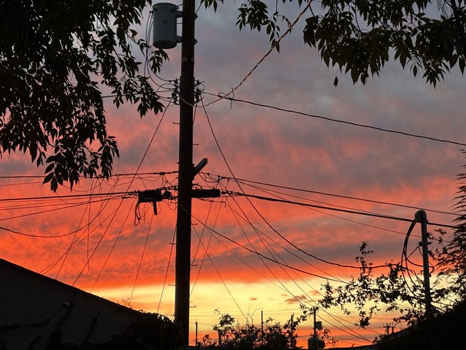 A dramatic sunset sky with pink and orange clouds silhouetted against utility poles and tangled power lines.