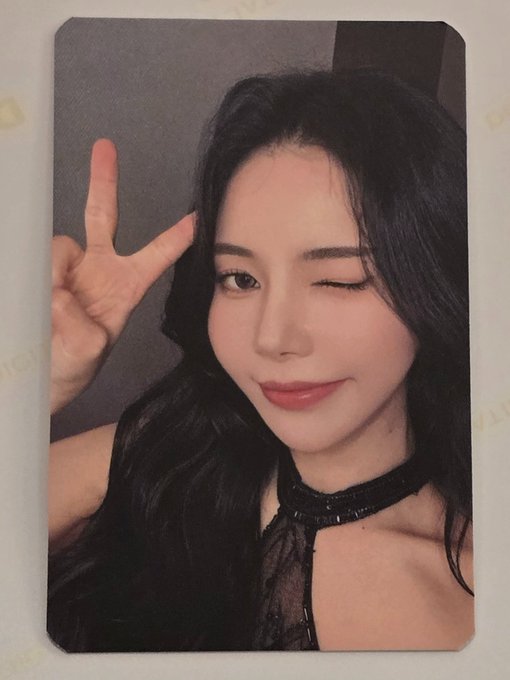 A woman with long dark hair wearing a black choker winks while making a peace sign in a selfie-style portrait with a polaroid-style border.