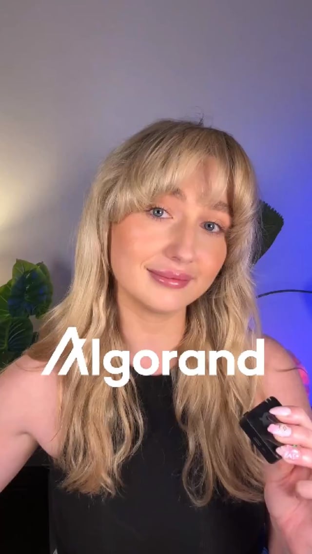 The image features a smiling woman with blonde hair holding a small device, with the "Algorand" logo prominently displayed, aligning with the post's message highlighting real-world utility growing on the Algorand platform despite a broader crypto market downturn.