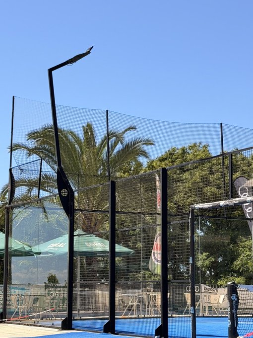 A clear blue sky overlooks an empty padel tennis court with a tall light pole, surrounded by protective netting and palm trees in the background. A "CROSSFIT" sign is partially visible behind the court, but no Solana address or ticker text appears in the image itself—the caption's reference to a "Solana address 👇" likely relates to the poster's promotional intent rather than anything shown visually.