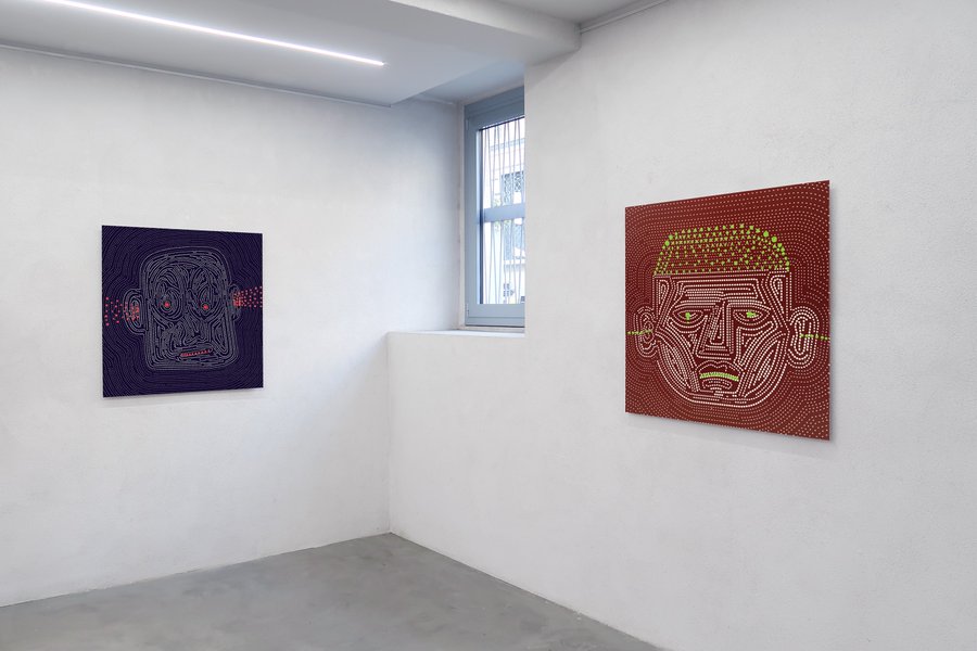 A minimalist white gallery space displaying two stylized, dot-patterned face artworks in purple and red/maroon tones on adjacent walls, with a window revealing an exterior building.