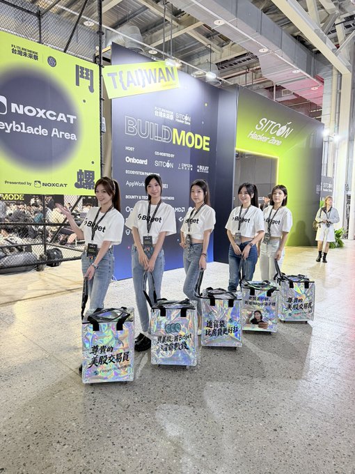 Five young women in white 'Bitget' t-shirts standing in a row at a 'BUILD MODE' event hosted by 'SITCON' in Taiwan, each standing behind a shopping bag.