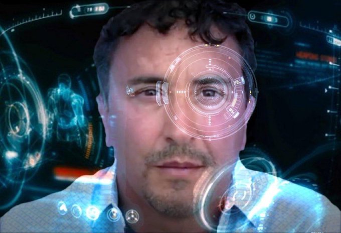 A cinematic still showing a man's face overlaid with futuristic glowing blue holographic HUD interfaces and targeting reticles, evoking a sci-fi or Iron Man-style heads-up display.