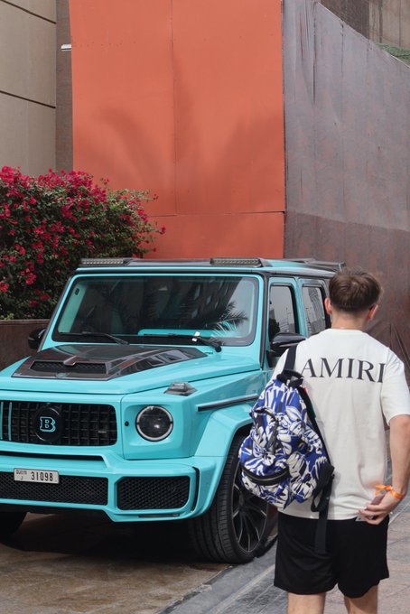 A man wearing an "AMIRI" t-shirt stands beside a turquoise Mercedes-Benz G-Class SUV with a UAE plate reading "31058." The post "GM GM GM" appears to reference the "G Wagon" Mercedes (often abbreviated as "G" or "G-Wagon"), making this image a fitting visual pun playing on the vehicle's nickname.