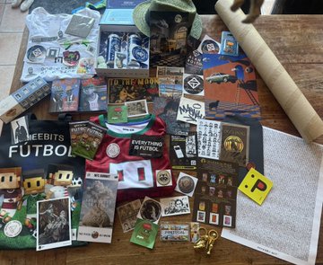 The image shows a table covered with various items, including stickers, magnets, books, and other knick-knacks. The objects are scattered across the surface of the table, creating an interesting visual display. In the background, there is a poster that reads "Minted and got the print Was so nice to meet you Alan Thank you". This text seems to be related to the items on the table or possibly part of a conversation about them.

The image does not provide any specific information about the content of the objects on the table, but it appears to be an assortment of personal items and souvenirs gathered together in one place.