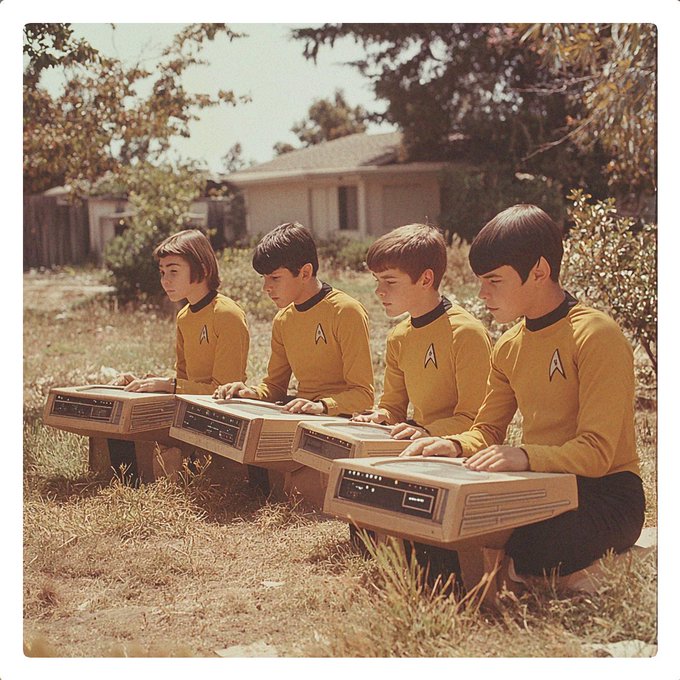 Four children wearing yellow Star Trek-style uniforms with the Starfleet insignia operate vintage computer terminals outdoors in a grassy yard.