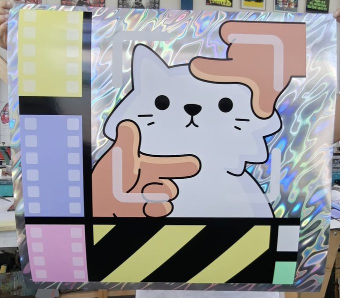 A colorful artwork on a holographic silver background featuring a cartoon white cat being held by a hand, alongside film strip motifs and geometric shapes in yellow, blue, pink, and black.