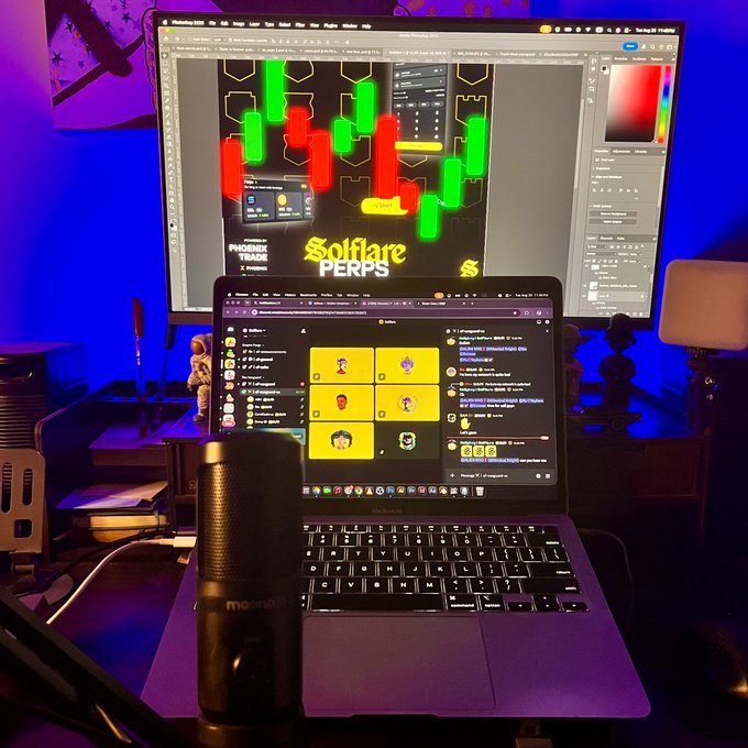A desk setup with a MacBook Pro in front of a monitor displaying cryptocurrency trading charts for "Solflare PERPS," with a Blue Yeti microphone in the foreground, illuminated by blue ambient lighting.