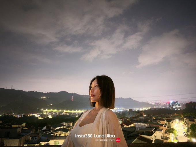 A young woman with shoulder-length dark hair stands overlooking a sprawling nighttime cityscape under a cloudy sky, with the text "Insta360 Luna Ultra" and "CO-ENGINEERED WITH Leica" overlaid at the bottom. The image directly promotes the #insta360lunaultra product, showcasing its low-light night photography capabilities to appeal to potential Luna fans.