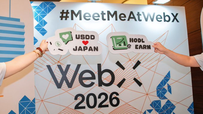 Two hands hold speech-bubble cutouts reading "USDD ❤️ JAPAN" and "HODL & EARN" in front of a "#MeetMeAtWebX" backdrop promoting "WebX 2026." The promotional signage ties into the post's theme of building yield within the USDD ecosystem, highlighting the conference as a venue where investors can explore sUSDD and advanced DeFi strategies like Pendle Finance.