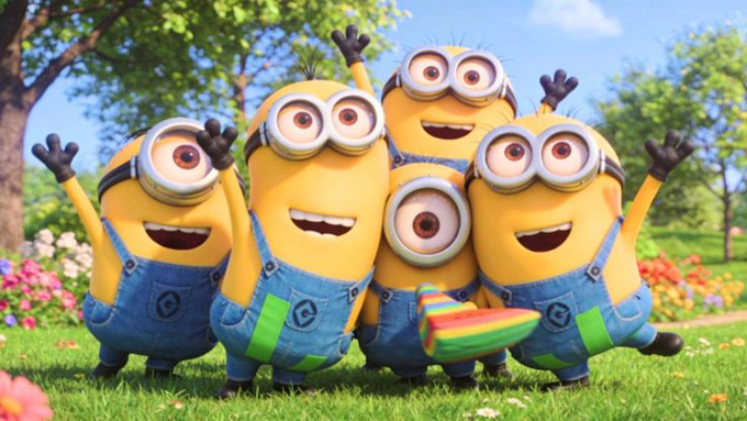 A group of cheerful Minions from the Despicable Me franchise posing in a sunny green field with colorful flowers, with one holding a rainbow-striped object.