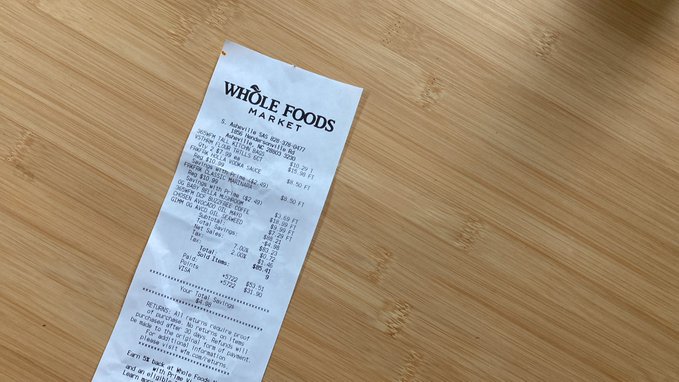 A Whole Foods Market receipt lies on a bamboo surface, with the store's name clearly visible at the top. The image humorously plays on the post's message about Bitcoin, suggesting that whether you own any Bitcoin or not, scanning your grocery receipt could be a worthwhile habit.