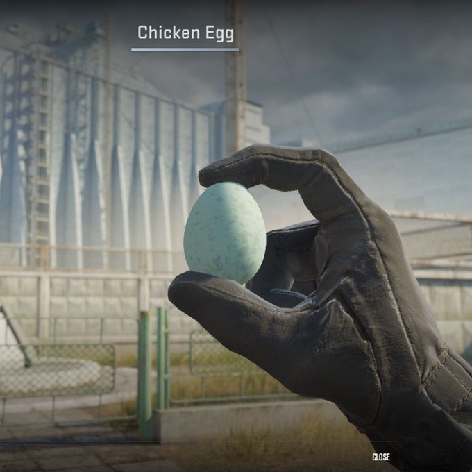 A video game screenshot showing a gloved hand holding a speckled blue egg labeled 'Chicken Egg' in front of industrial silos, with 'CLOSE' in the corner.