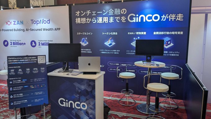 A trade show booth for 'Ginco,' a ZAN x Topliod partnership booth promoting an AI-Powered, AI-Secured Wealth App and on-chain finance services, featuring displays, monitors, and high-top seating.