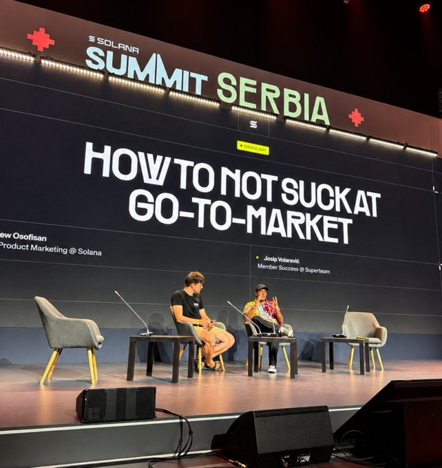 Two people sit on stage at the Solana Summit Serbia during a panel titled 'How to Not Suck at Go-to-Market,' featuring speakers from Solana and Superteam.