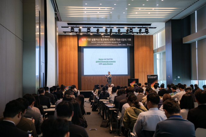 A speaker presents to a packed auditorium during the "원화기반 실물자산 토큰화의 시도와 자산토큰화의 기획" (KRW-based Real World Asset Tokenization Initiatives) event, with a slide reading "Korea can lead the global financial economy with open finance." The image illustrates the conference described in the post, where around 300 finance industry representatives gathered at the Deloitte Korea and Tiger Research event—sponsored by Plume—to discuss tokenizing Korean assets onchain.