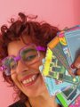 A low-resolution pixelated avatar of a person with curly reddish hair and pink sunglasses smiling enthusiastically while holding a colorful item.