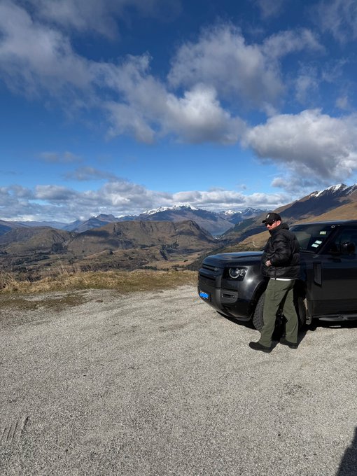 A man stands beside a black Mazda pickup truck on a gravel overlook, gazing out at a sweeping mountain valley under a partly cloudy sky—a serene, free-spirited moment that visually embodies the post's "fuck the markets" sentiment of stepping away from stocks and Forex to embrace the freedom crypto and memecoins promise.