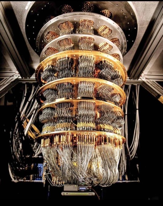 A close-up view of a complex piece of scientific equipment, possibly a dilution refrigerator used in quantum computing, featuring stacked gold-colored discs with numerous wires and cables extending from them.