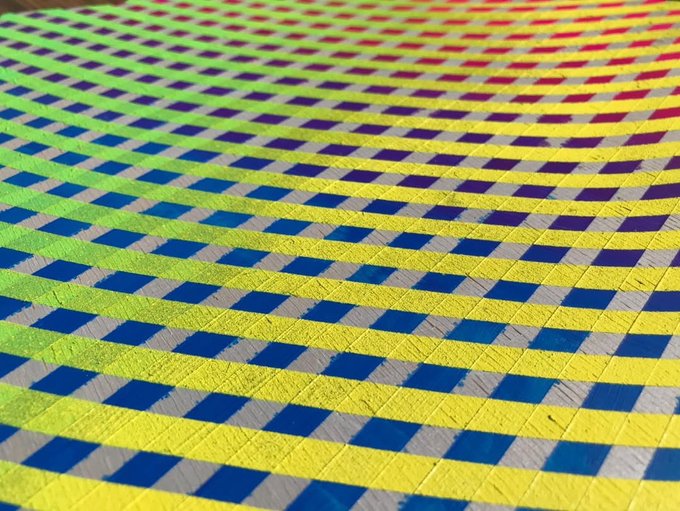 A colorful woven textile pattern featuring a grid of yellow, blue, green, red and silver squares creating a vibrant geometric design