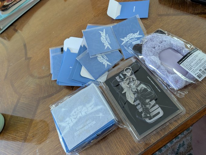 A "Stray Kids" 2025 Season's Greetings merchandise set is unpacked on a wooden table, featuring blue card packs, a photobook with member artwork, a "SKZ" plush keychain, and other collectibles—signaling the arrival of the new year's fan package.