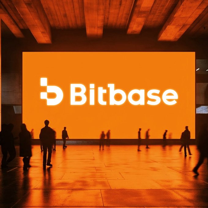 A massive orange-lit billboard displaying the "Bitbase" logo dominates a cavernous hall, with silhouetted figures moving across the polished floor below. The glowing screen serves as a steady beacon amid the flowing crowd and shifting shadows, embodying the post's message of being a constant anchor in an ever-changing landscape.